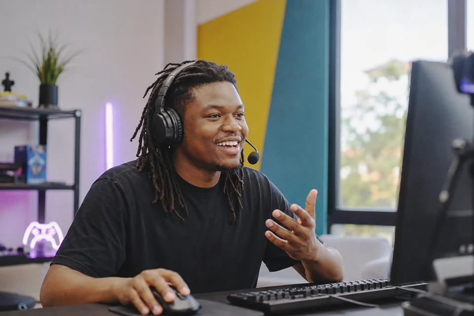 A smiling South African caster with a headset commentating at a gaming PC